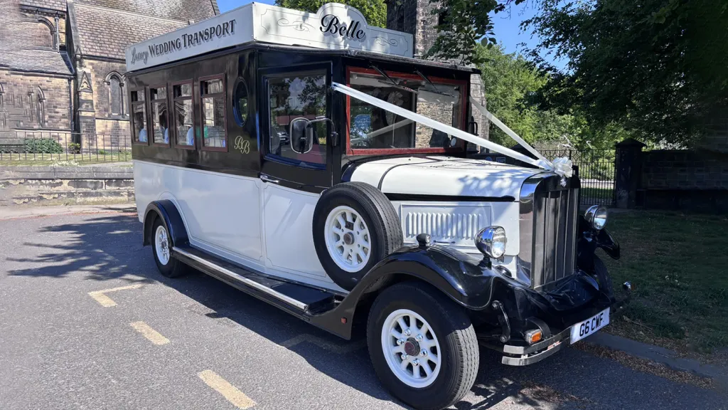 Black and Ivory vintage Asquith bus decorated with white wedding ribbons parked in front of church in Leeds