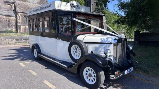 Black and Ivory vintage Asquith bus decorated with white wedding ribbons parked in front of church in Leeds