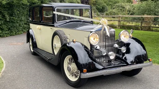 1935 black and ivory Rolls-Royce 20/25 vintage wedding car parked on driveway decorated with ivory ribbons and front headlights on
