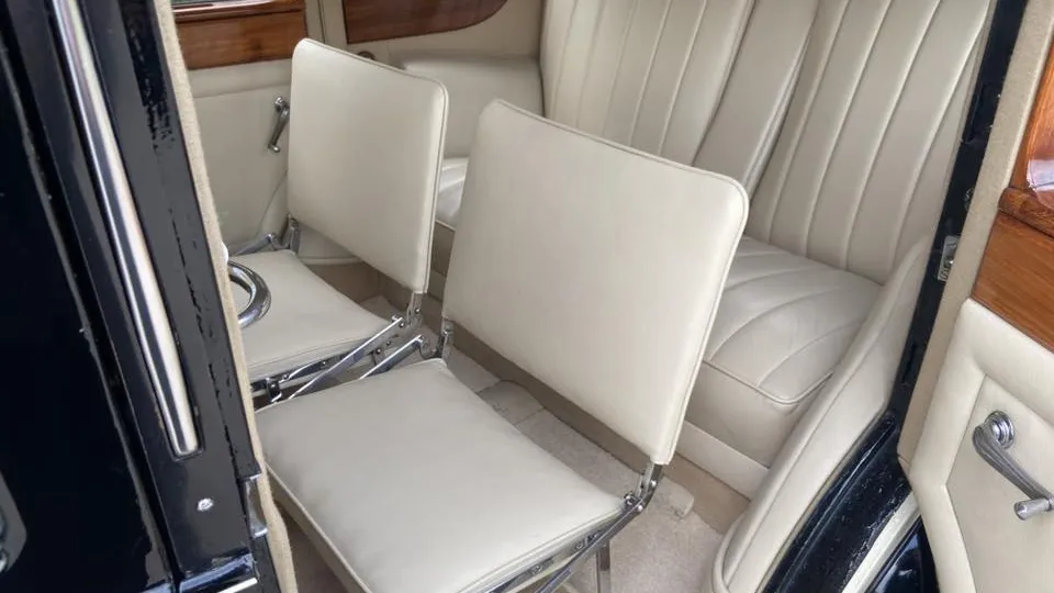 Fold-down occasional seats raised inside the rear cabin of a vintage Rolls-Royce with cream leather interior