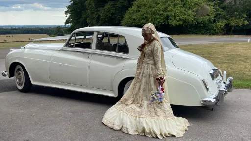 Asian bride standing behind a white Rolls-Royce Silver Cloud with her dress flowing on the ground