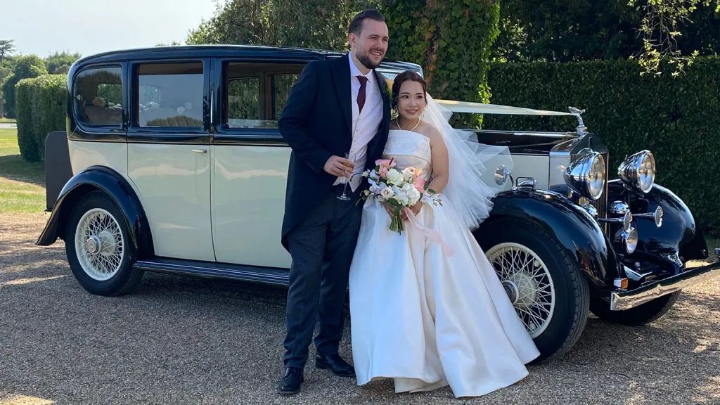 Bride and groom standing beside a black and ivory vintage Rolls-Royce 20/25