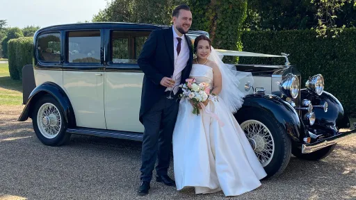 Bride and groom standing beside a black and ivory vintage Rolls-Royce 20/25