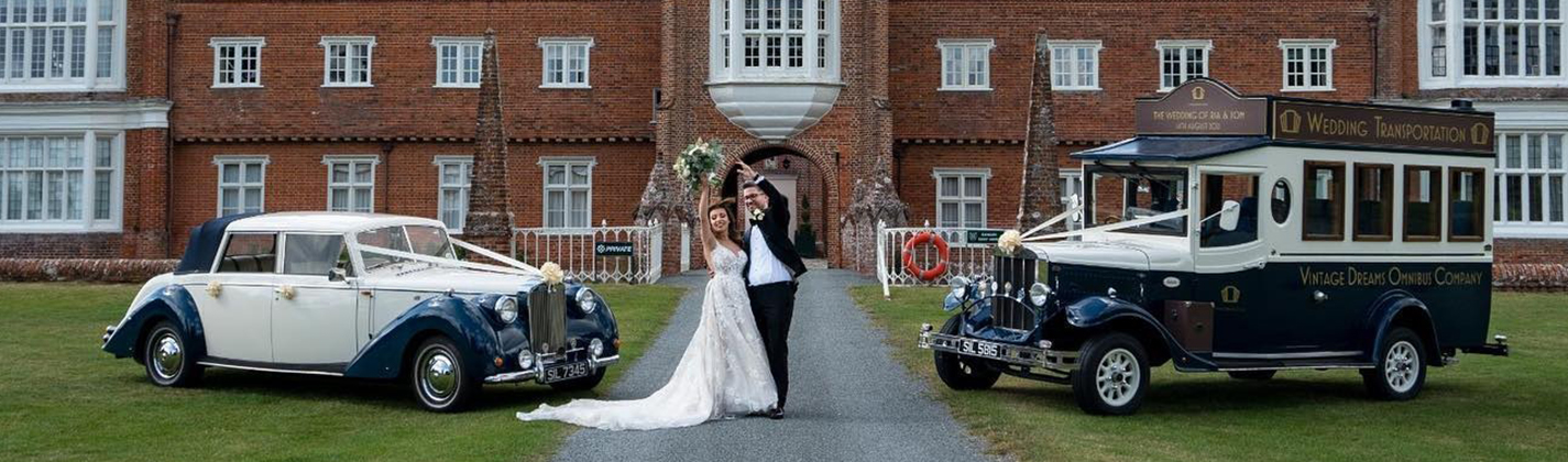 A Classic blue car and a vintage bus in blue parked in the garden of a large wedding venue with Bride and Groom standing in the middle of both vehicles