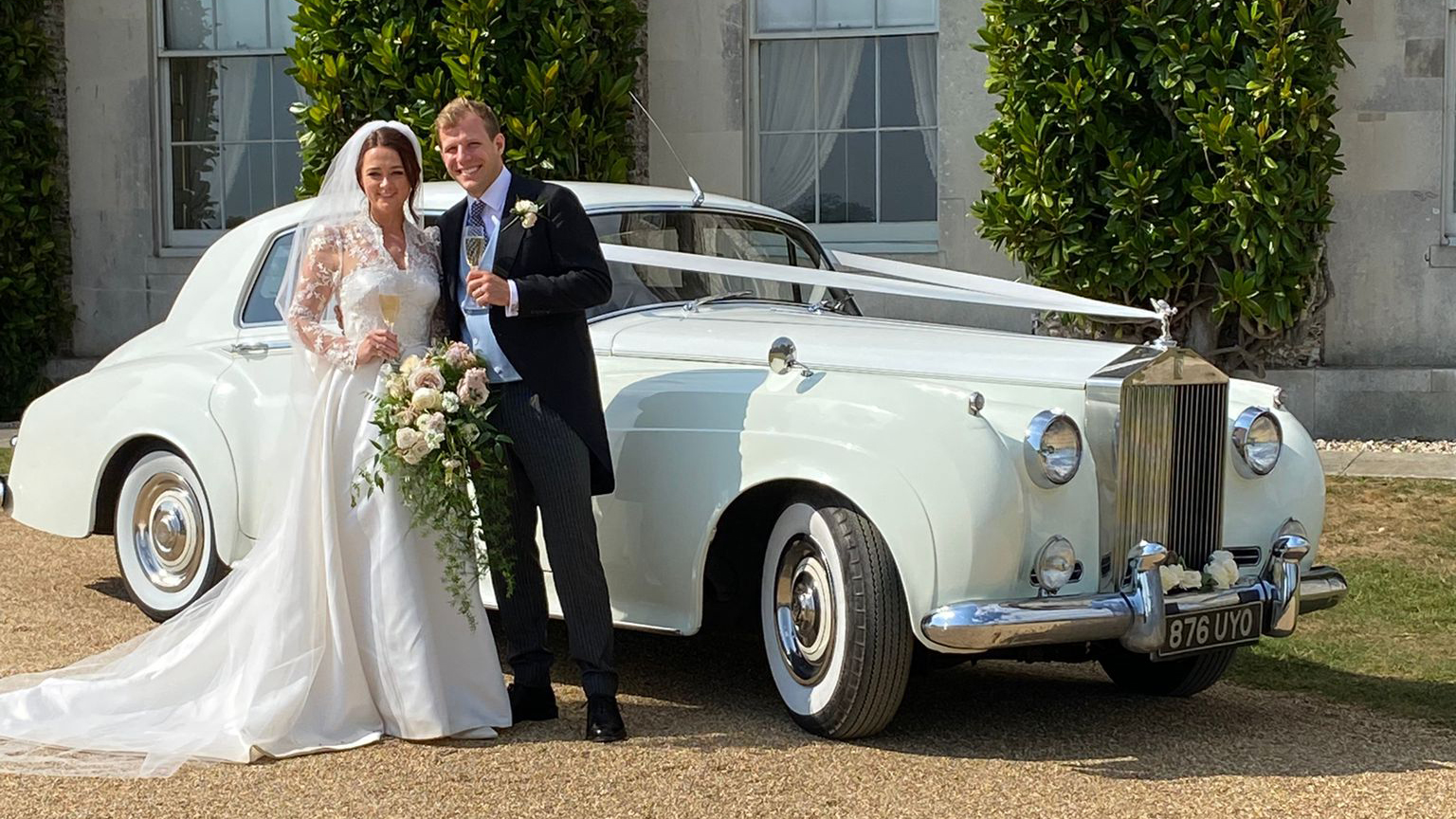 Bride and groom posing together beside a white Rolls-Royce Silver Cloud
