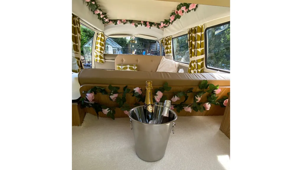 Interior view of a classic VW campervan seen from the open rear boot door with champagne bucket and floral garland