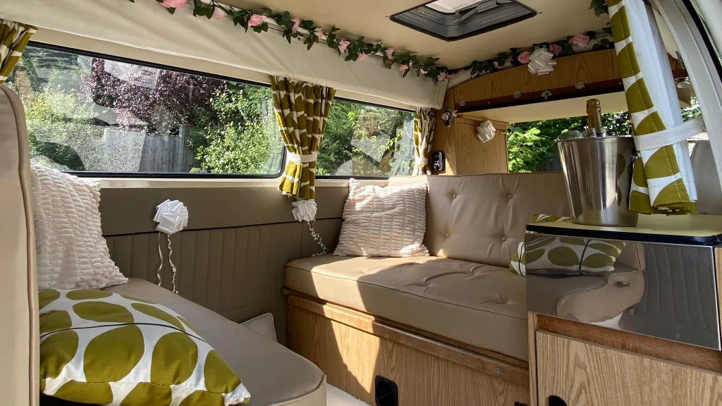Cosy rear lounge area in a classic VW campervan with scatter cushions and wooden cabinets