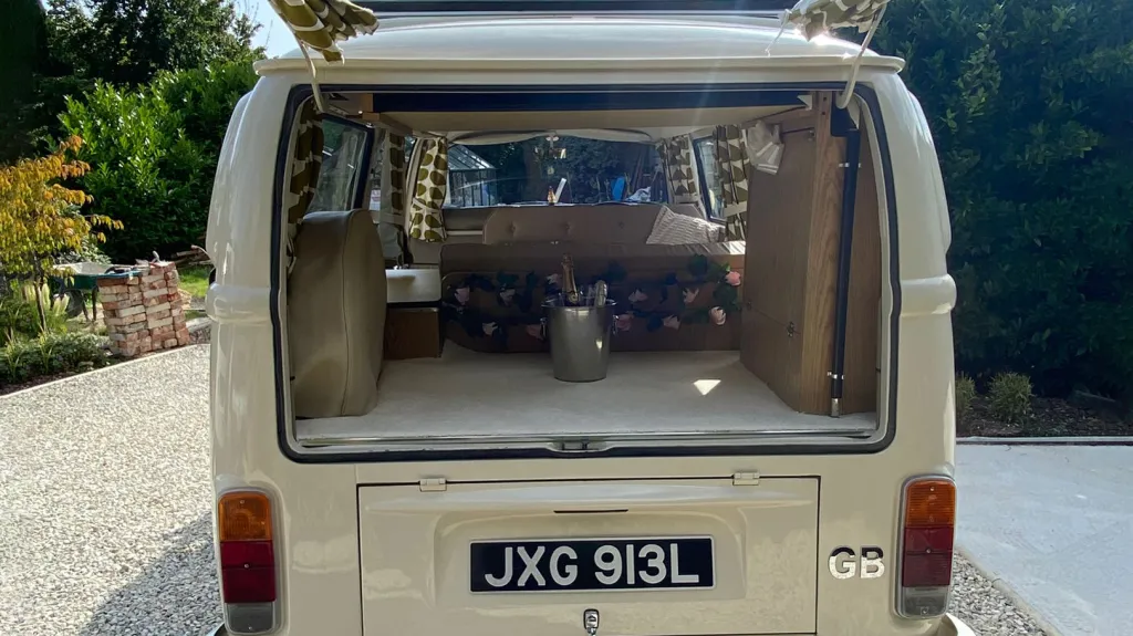 Open rear hatch of a classic VW campervan showing parcel shelf and decorated interior