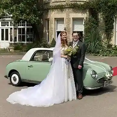 Bride and groom posing with a pale green Nissan Figaro classic car
