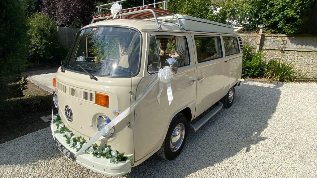 Cream classic VW campervan decorated with flowers parked in the sun