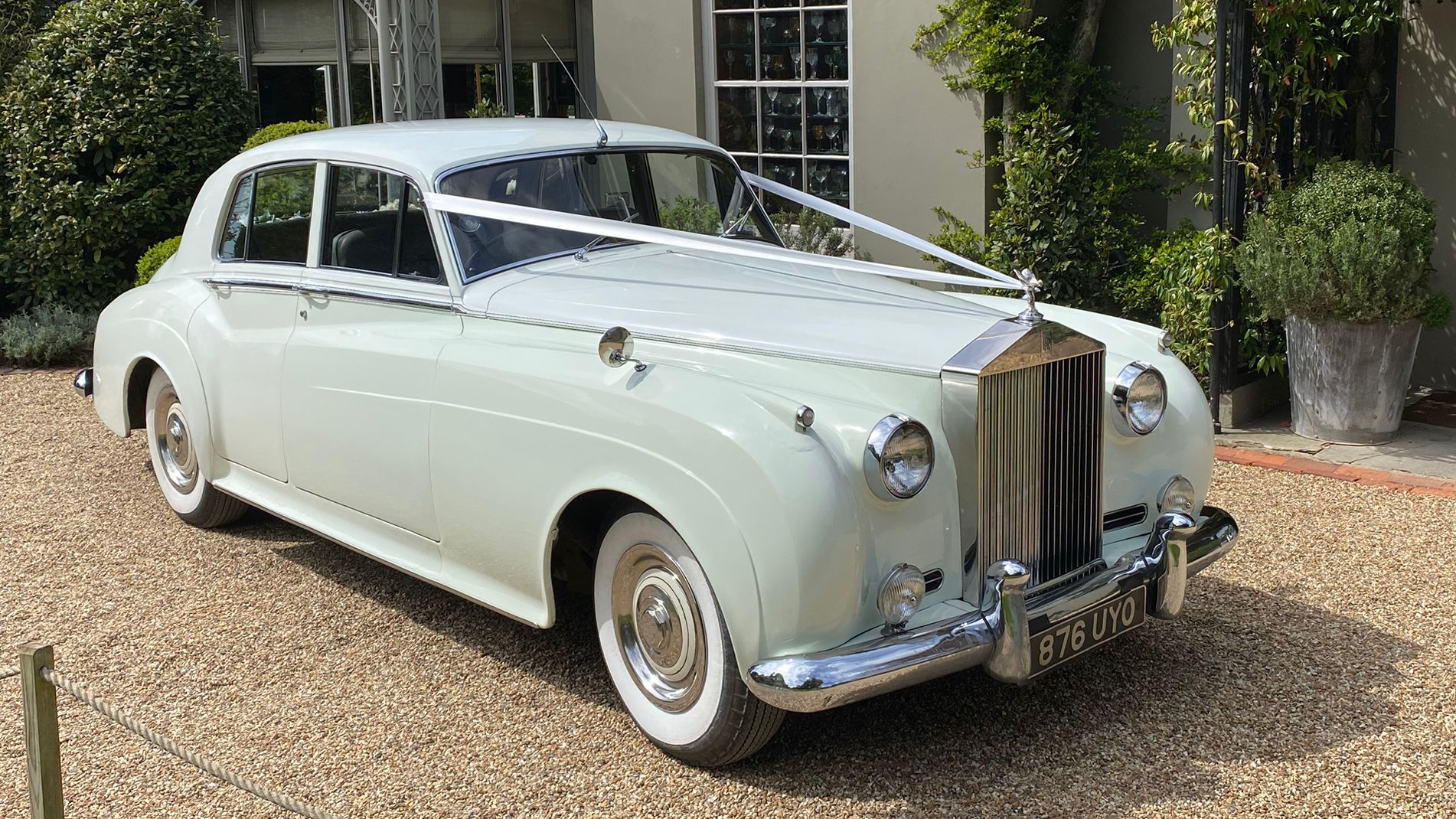 White Rolls-Royce Silver Cloud wedding car with ribbons parked on gravel outside a country house