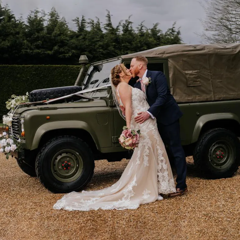 Bride and groom kissing in front of an army green Willys Jeep with wedding flowers