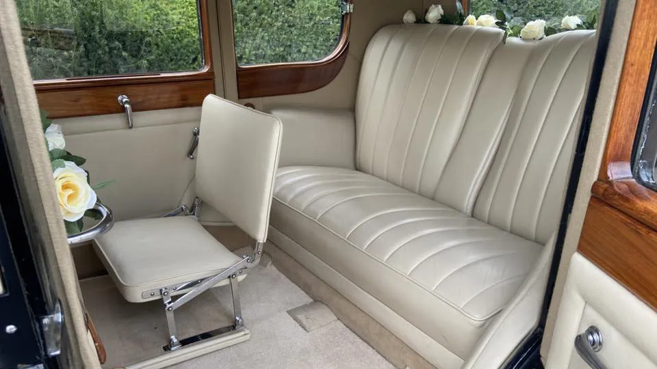 Cream leather rear seats inside a vintage Rolls-Royce 20/25 limousine with one of the casual seat up