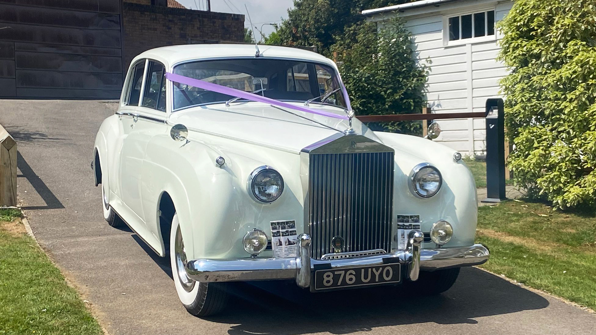 Front view of a white Rolls-Royce Silver Cloud with purple wedding ribbons across the bonnet