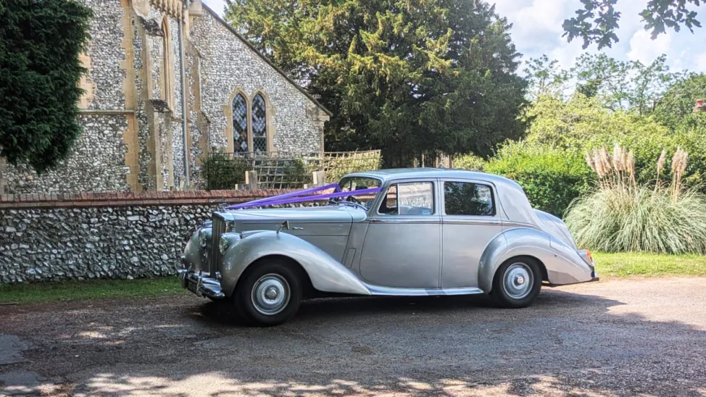 Left side profile of a silver Bentley R-Type parked outside a stone church