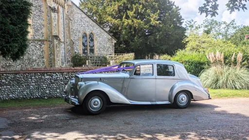 Left side profile of a silver Bentley R-Type parked outside a stone church