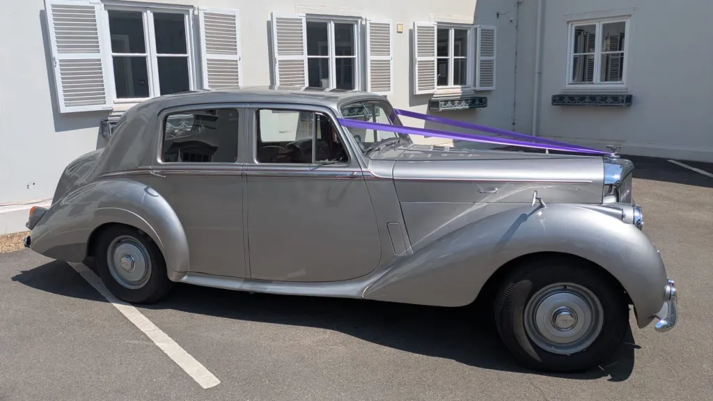 Right side view of a silver Bentley R-Type decorated with purple wedding ribbons