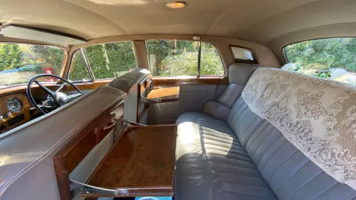 Interior of a Rolls-Royce Silver Cloud showing grey leather seats and polished wood trim