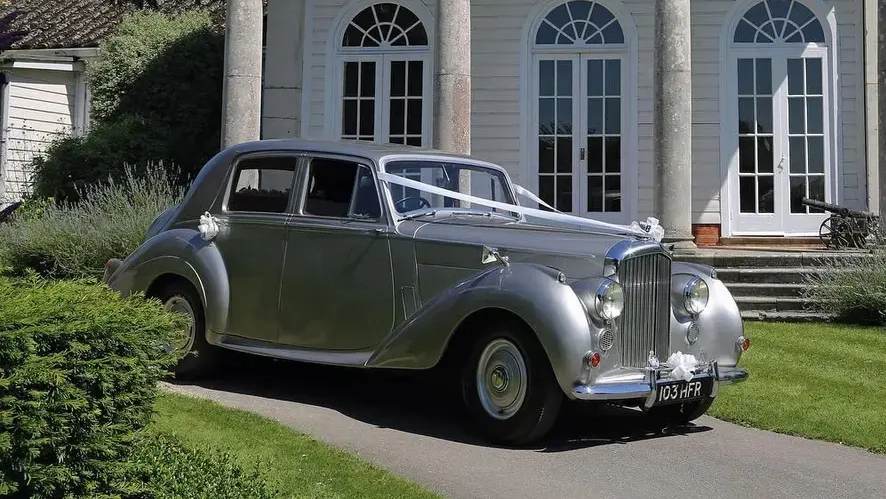 Silver Bentley R-Type classic car parked on grass outside a wedding venue