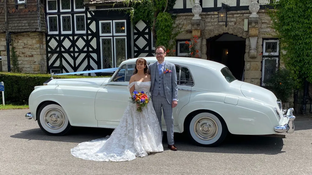 Wedding couple standing arm in arm next to a white Rolls-Royce Silver Cloud