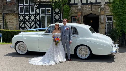 Wedding couple standing arm in arm next to a white Rolls-Royce Silver Cloud