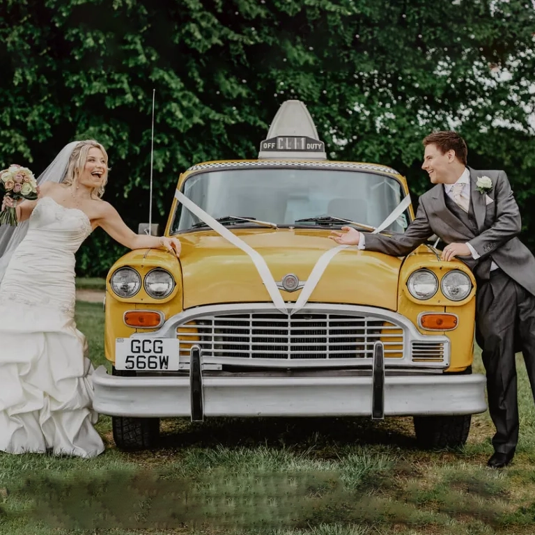 Bride and groom playfully posing with a classic American yellow taxi cab wedding car.