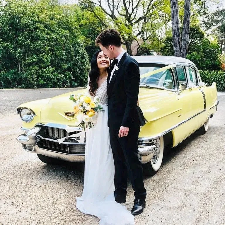 Wedding couple standing in front of a bright yellow Cadillac wedding car holding a bouquet.