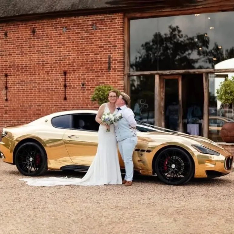 Couple in wedding attire posing with a striking gold Maserati supercar hire.
