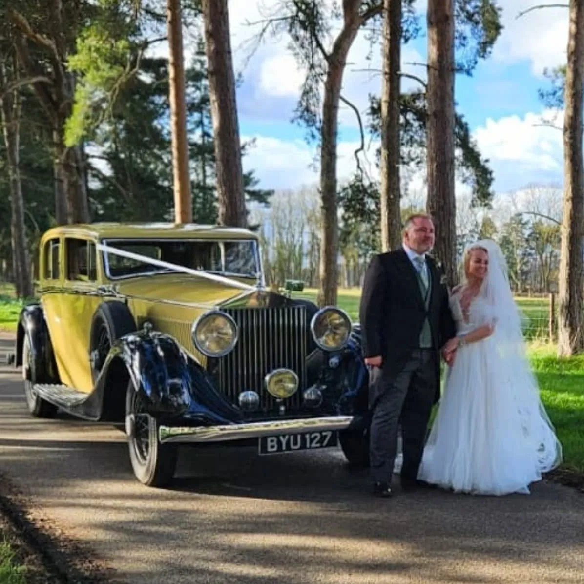 Bride and groom with a yellow vintage Rolls-Royce wedding car on a sunny wedding day.