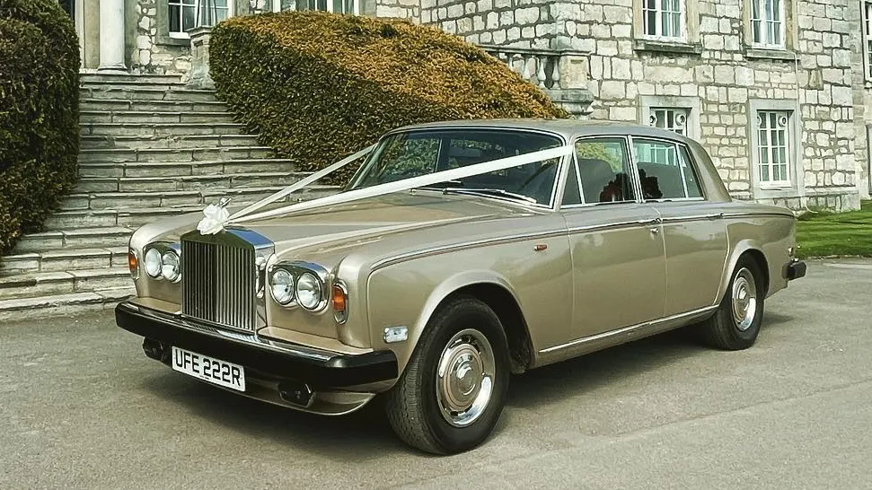 Front side view of a gold Rolls-Royce Silver Shadow outside a grand building, available for wedding hire in Yorkshire.