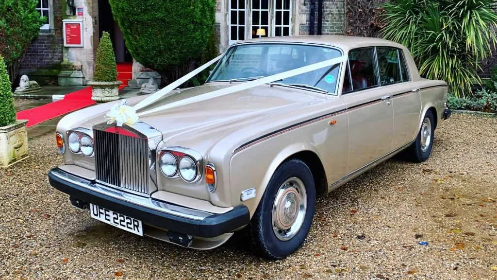 Gold Rolls-Royce Silver Shadow decorated with white wedding ribbons outside a venue, available for wedding hire in Yorkshire.