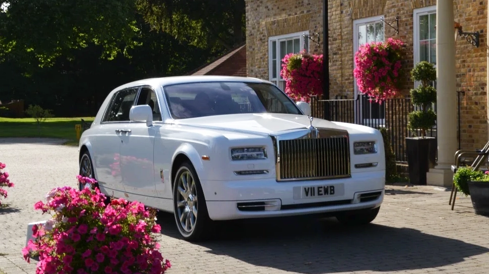 Right side view of White Rolls-Royce Phantom 7 series 2 Extended Wheelbase with pink flowers in the background