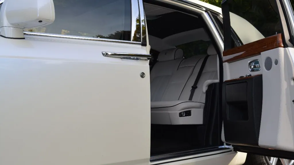 Rolls-Royce Phantom rear passenger door open showing white leather interior with wooden features on top of the door card
