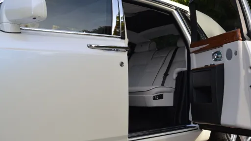 Rolls-Royce Phantom rear passenger door open showing white leather interior with wooden features on top of the door card
