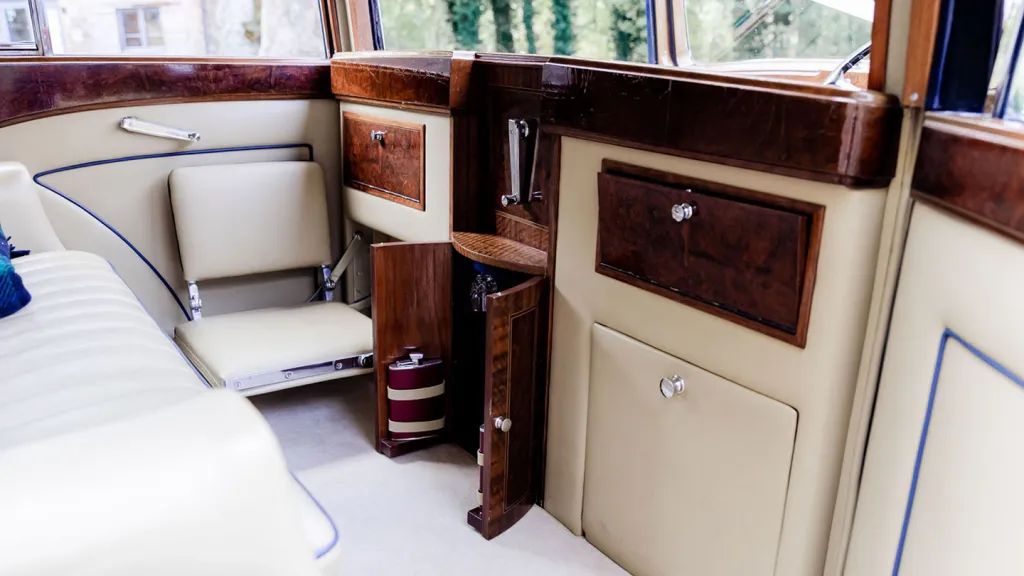 Luxurious cream leather and polished wood rear cabin interior inside a vintage Rolls-Royce with one of the casual seat open
