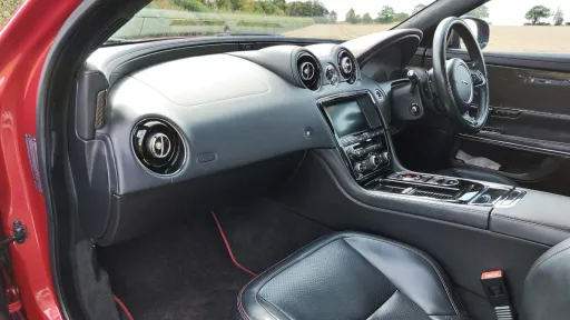 Close-up of the cockpit and dashboard inside a Jaguar XJR, showing a black leather interior with chrome and gloss black trim.