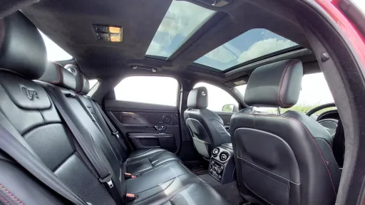 Rear cabin view of a Jaguar XJR featuring spacious black leather seating and a panoramic glass sunroof letting in natural light.