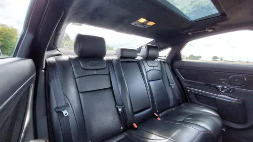 Rear passenger seats of a Jaguar XJR, finished in luxurious black leather with visible headrests and central armrest.