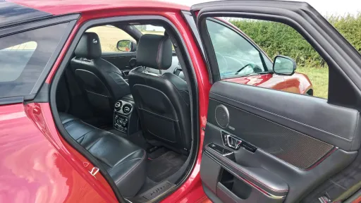 Rear passenger door open on a red Jaguar XJR, revealing black leather interior seating and modern trim details.