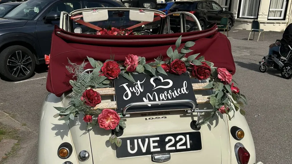 Rear view opf Morris Minor Convertible on wedding duties with "Just Married" sign and red roses floral decoration around the sign