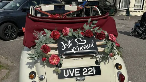 Rear view opf Morris Minor Convertible on wedding duties with "Just Married" sign and red roses floral decoration around the sign