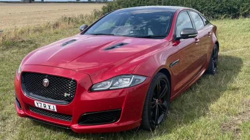 Front angled view of a red Jaguar XJR parked on grass, showing its bold grille, black alloy wheels and sporty stance.