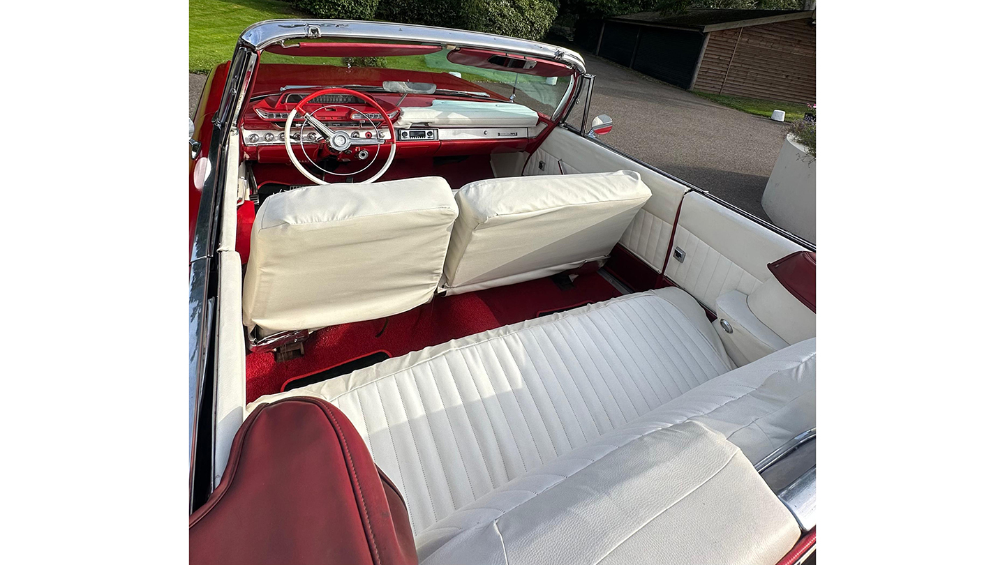 Interior of a classic red Dodge convertible showing white leather seats with red trim and a red dashboard.