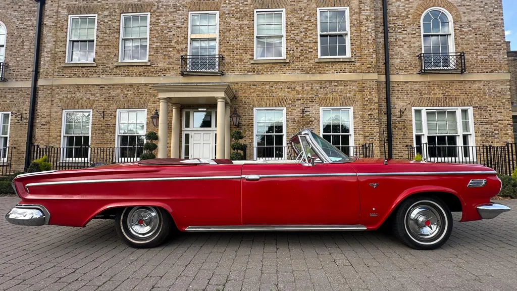 Side profile of a red Dodge classic convertible parked outside a traditional brick townhouse wedding venue.
