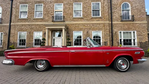 Side profile of a red Dodge classic convertible parked outside a traditional brick townhouse wedding venue.