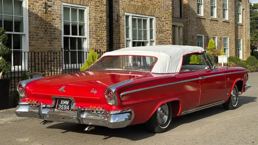 Rear angled view of a red Dodge convertible with a white soft-top roof, parked in front of an elegant brick townhouse.