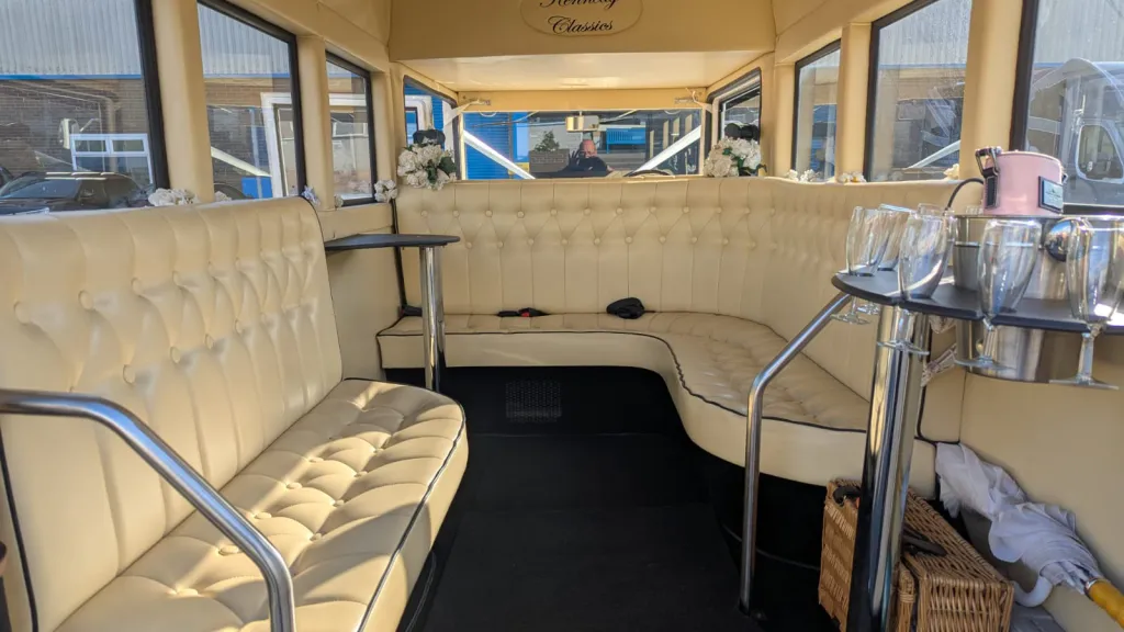 Interior of an Imperial wedding bus featuring cream leather bench seating with chrome handrails and large windows.