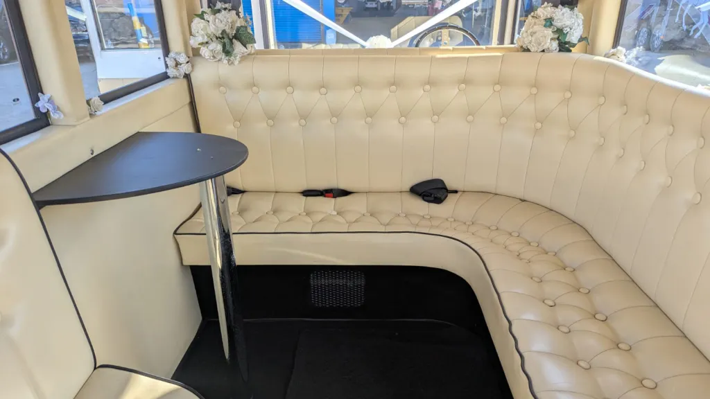 Spacious cream leather interior of an Imperial vintage bus with corner seating and polished black flooring.