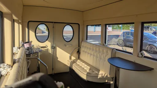 Inside view of an Imperial vintage wedding bus showing round windows, cream seating and a small side table.