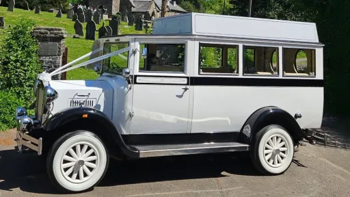 Left side exterior view of a white Imperial wedding bus with contrasting black panels, parked on grass beside trees.